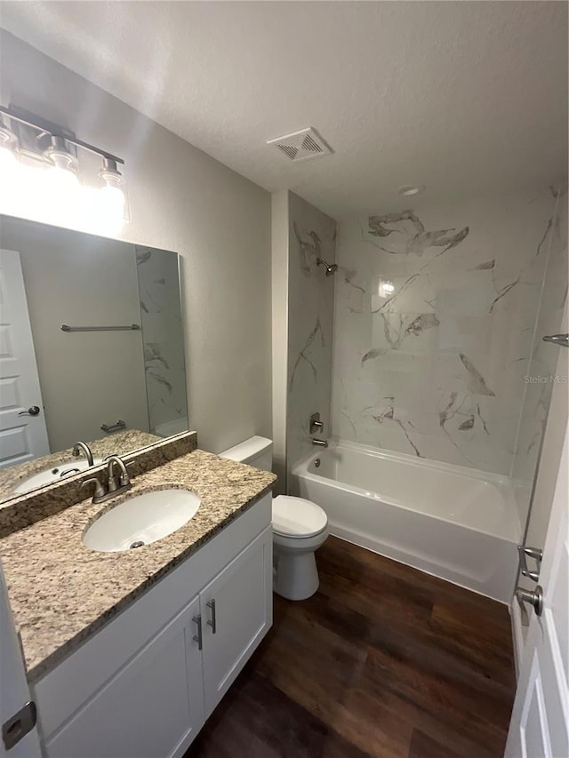 full bathroom featuring hardwood / wood-style floors, tiled shower / bath combo, a textured ceiling, vanity, and toilet