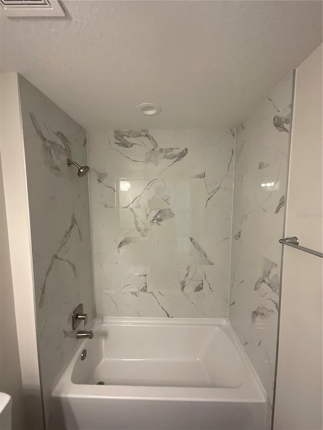 bathroom with tiled shower / bath and a textured ceiling