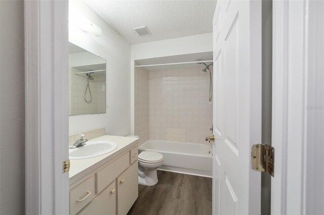 full bathroom featuring hardwood / wood-style flooring, vanity, a textured ceiling, toilet, and tiled shower / bath