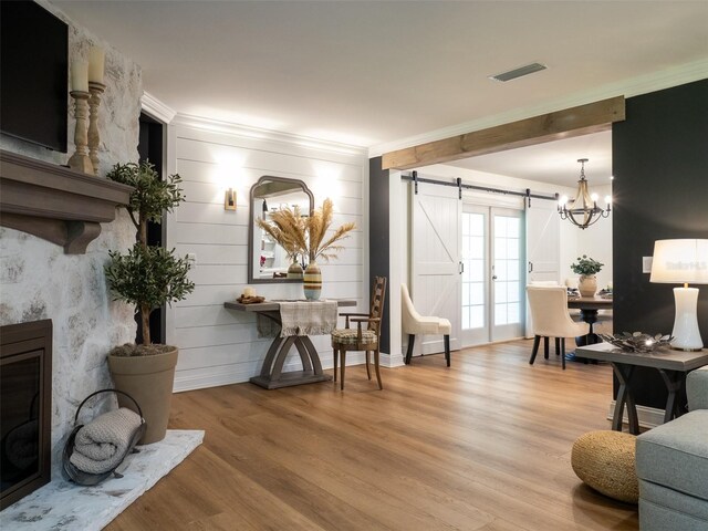 living room featuring ornamental molding, a barn door, a chandelier, and light hardwood / wood-style floors