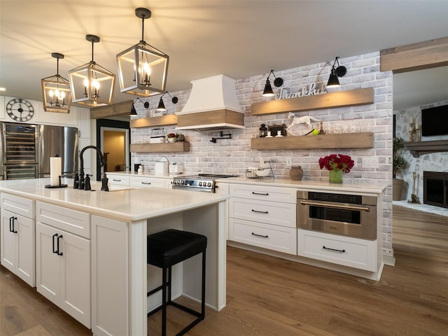 kitchen featuring dark hardwood / wood-style floors, white cabinets, custom range hood, an island with sink, and stainless steel appliances