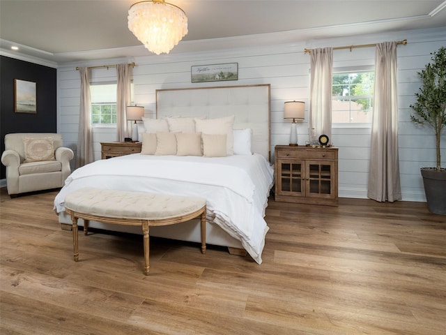 bedroom featuring a notable chandelier, wood-type flooring, multiple windows, and ornamental molding