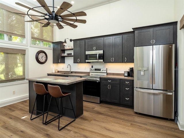 kitchen featuring ceiling fan, appliances with stainless steel finishes, a center island, light wood-type flooring, and a breakfast bar area