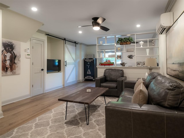 living room with ceiling fan, a barn door, light wood-type flooring, and an AC wall unit