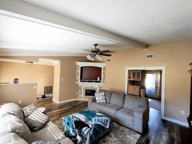 living room with lofted ceiling with beams, a stone fireplace, ceiling fan, and dark wood-type flooring