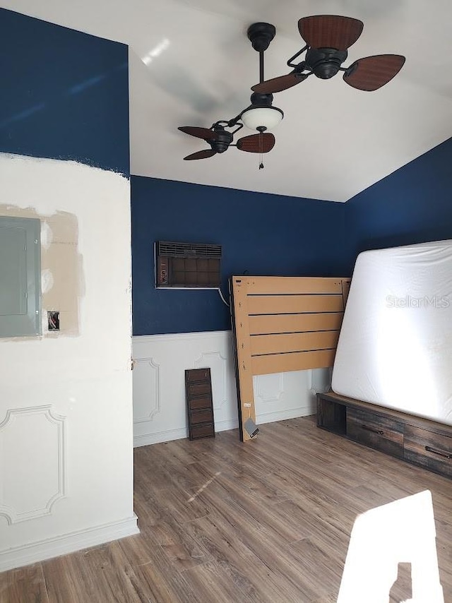 unfurnished bedroom featuring hardwood / wood-style flooring, ceiling fan, an AC wall unit, and electric panel