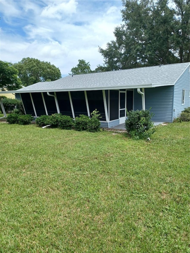 rear view of house featuring a sunroom, a shingled roof, and a lawn