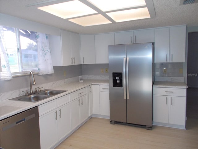 kitchen with appliances with stainless steel finishes, white cabinets, sink, and light hardwood / wood-style floors