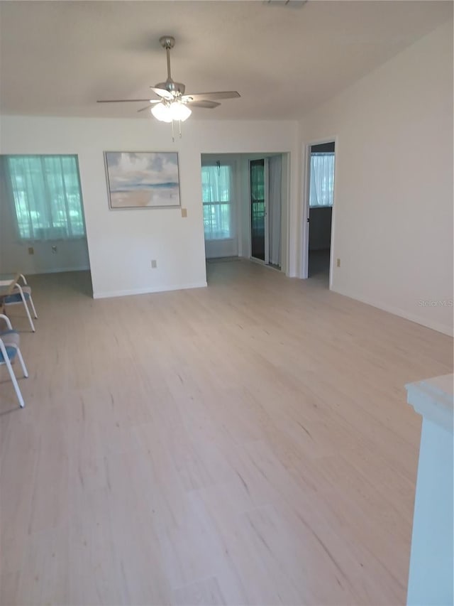 unfurnished living room with ceiling fan, light wood-style flooring, and baseboards