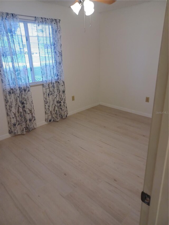 empty room with ceiling fan, light wood-type flooring, and baseboards