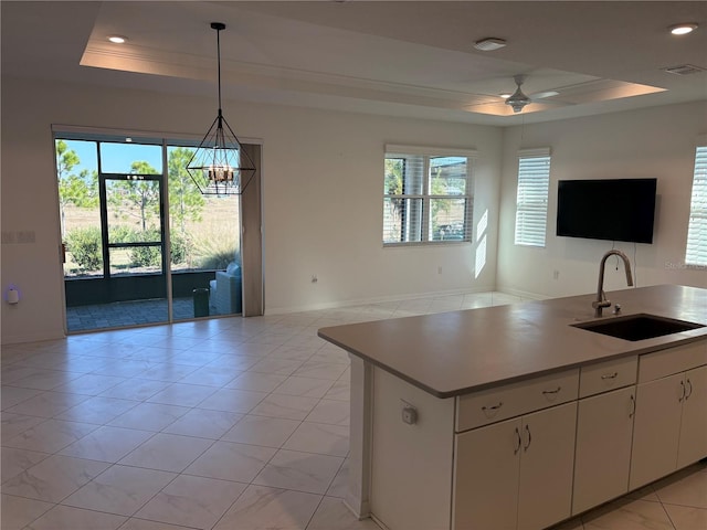 kitchen featuring a raised ceiling, white cabinetry, sink, and a healthy amount of sunlight