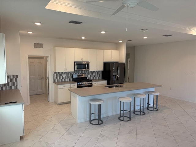 kitchen with a kitchen island with sink, white cabinets, sink, decorative backsplash, and stainless steel appliances