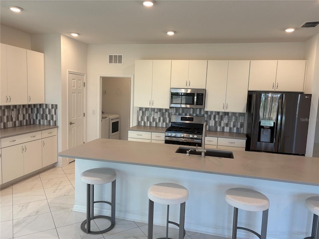 kitchen featuring white cabinets, a kitchen bar, appliances with stainless steel finishes, and tasteful backsplash