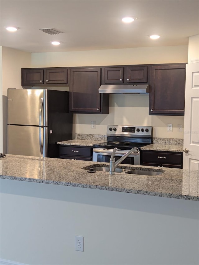 kitchen featuring appliances with stainless steel finishes, sink, dark brown cabinetry, and light stone countertops