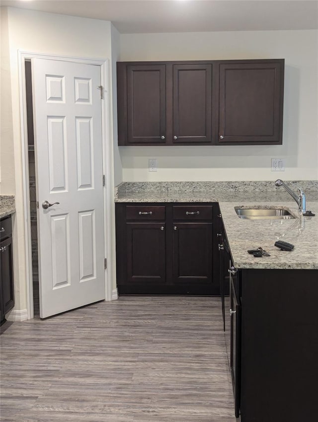 kitchen with sink, light hardwood / wood-style flooring, dark brown cabinets, and light stone countertops