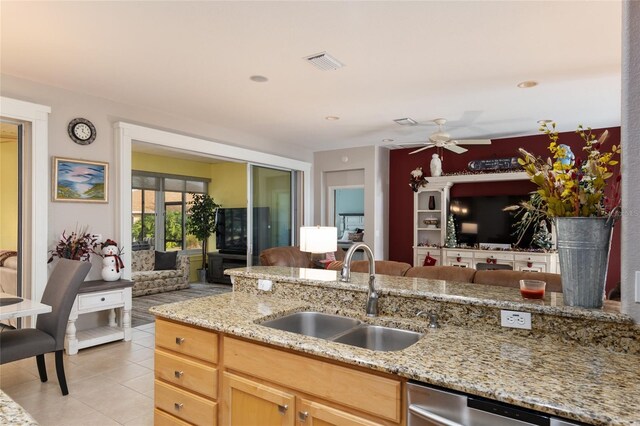 kitchen with light tile patterned floors, light brown cabinets, light stone counters, ceiling fan, and sink