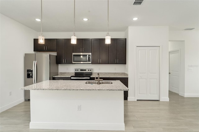 kitchen with stainless steel appliances, light stone counters, a kitchen island with sink, and sink