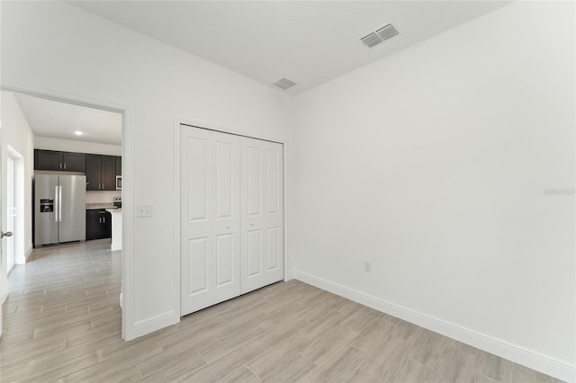 unfurnished bedroom with stainless steel fridge with ice dispenser, a closet, and light wood-type flooring