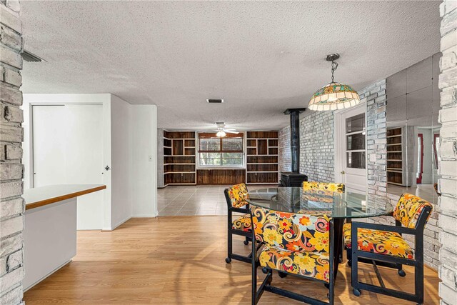 dining area with light hardwood / wood-style flooring, a textured ceiling, built in shelves, a wood stove, and ceiling fan