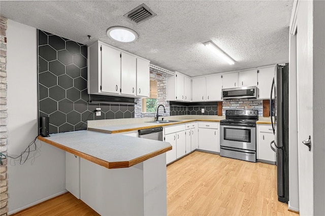 kitchen featuring stainless steel appliances, light hardwood / wood-style flooring, kitchen peninsula, and decorative backsplash