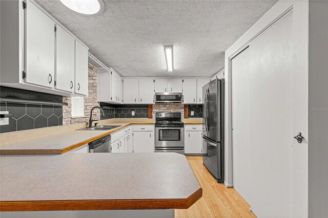 kitchen with decorative backsplash, light hardwood / wood-style flooring, appliances with stainless steel finishes, kitchen peninsula, and sink