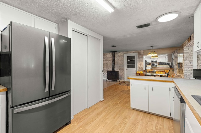 kitchen with a textured ceiling, white cabinetry, appliances with stainless steel finishes, a wood stove, and light wood-type flooring