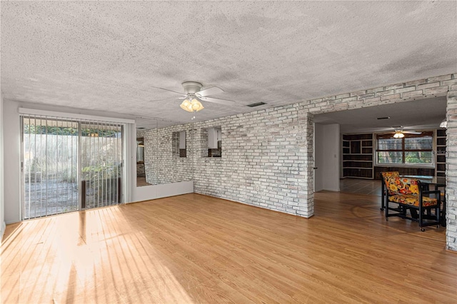 empty room with ceiling fan, hardwood / wood-style flooring, a textured ceiling, and brick wall