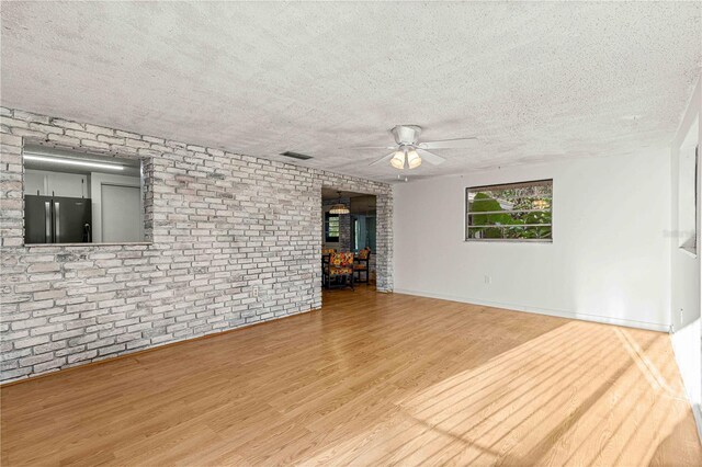 unfurnished living room with ceiling fan, light hardwood / wood-style flooring, a textured ceiling, and brick wall