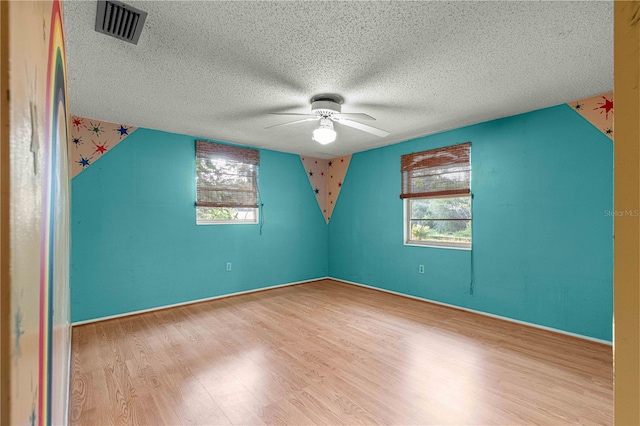 empty room featuring light wood-type flooring, a textured ceiling, and a healthy amount of sunlight