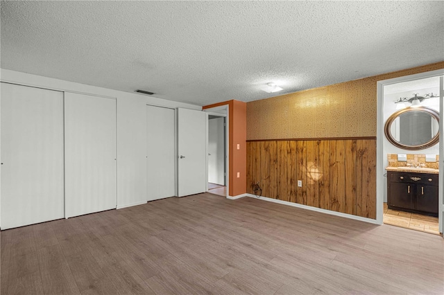 unfurnished bedroom with a textured ceiling, wood-type flooring, sink, and connected bathroom