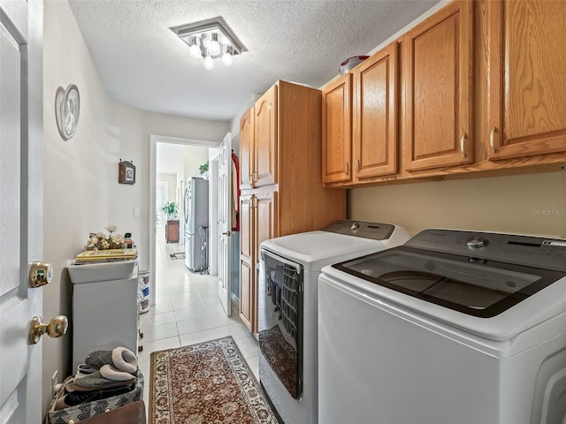 laundry area featuring cabinet space, washing machine and dryer, a textured ceiling, and light tile patterned flooring