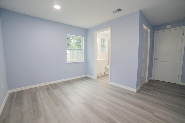 unfurnished bedroom with ensuite bath and light wood-type flooring