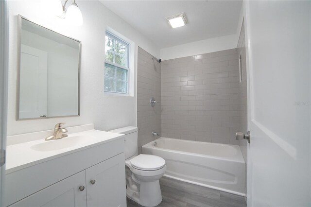 full bathroom with tiled shower / bath combo, vanity, hardwood / wood-style flooring, and toilet