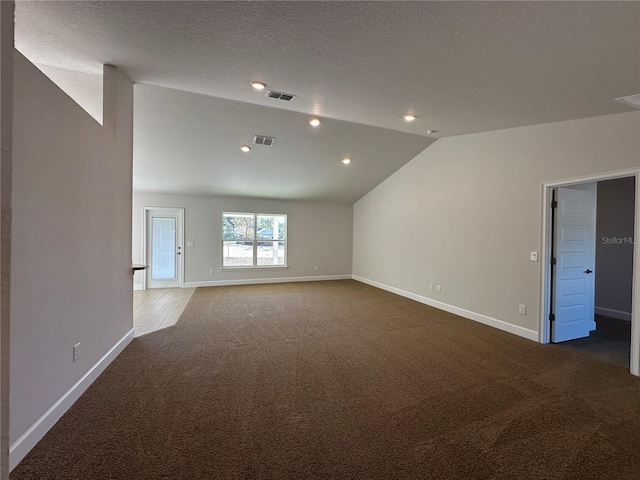 unfurnished room with a textured ceiling, lofted ceiling, and dark colored carpet