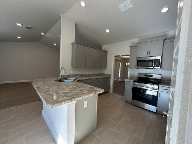 kitchen with gray cabinetry, sink, vaulted ceiling, kitchen peninsula, and stainless steel appliances