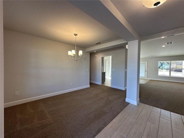 carpeted empty room featuring a textured ceiling and a chandelier