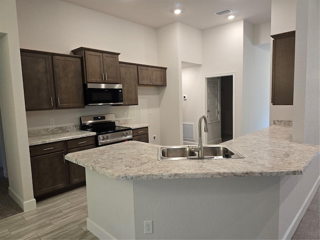 kitchen with sink, dark brown cabinets, stainless steel appliances, light stone counters, and kitchen peninsula