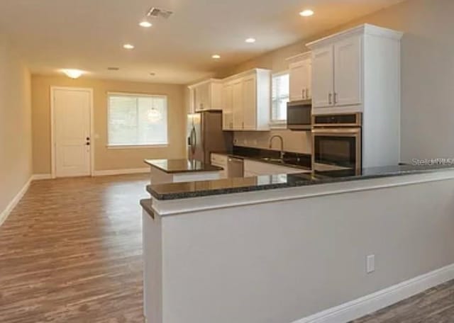 kitchen with kitchen peninsula, dark hardwood / wood-style floors, appliances with stainless steel finishes, and white cabinetry