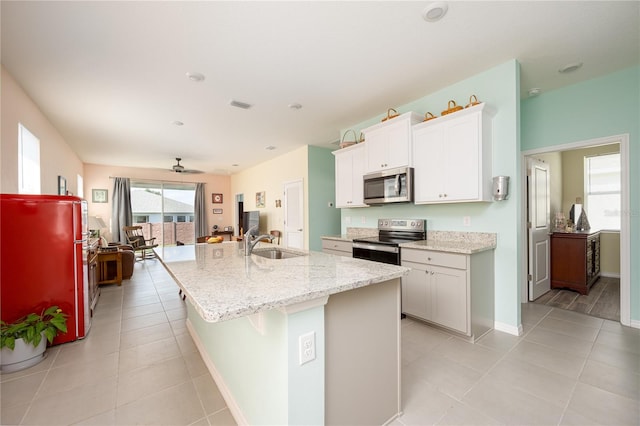 kitchen with appliances with stainless steel finishes, an island with sink, sink, white cabinetry, and light tile patterned flooring