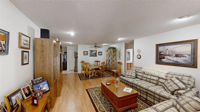 living room with ceiling fan, light wood-type flooring, and a textured ceiling