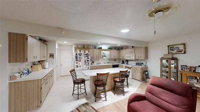 kitchen with a textured ceiling, light wood-type flooring, white appliances, sink, and a breakfast bar area