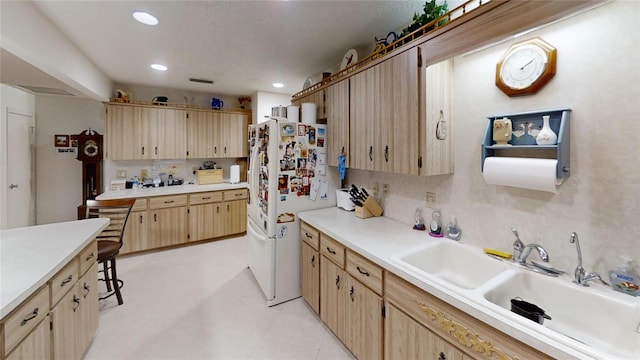 kitchen with a textured ceiling, light brown cabinets, white refrigerator, light tile patterned floors, and sink