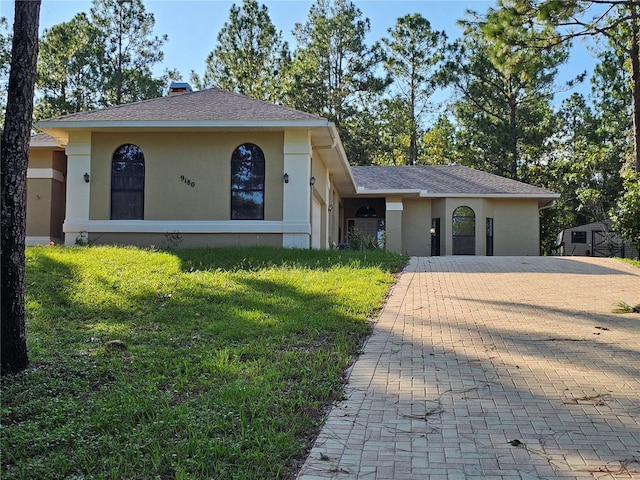 view of front facade with a front yard, roof with shingles, a chimney, and stucco siding