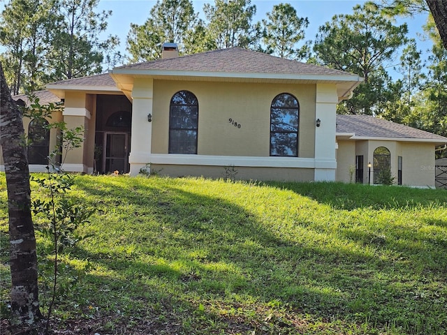 view of front of house with a front yard, roof with shingles, a chimney, and stucco siding