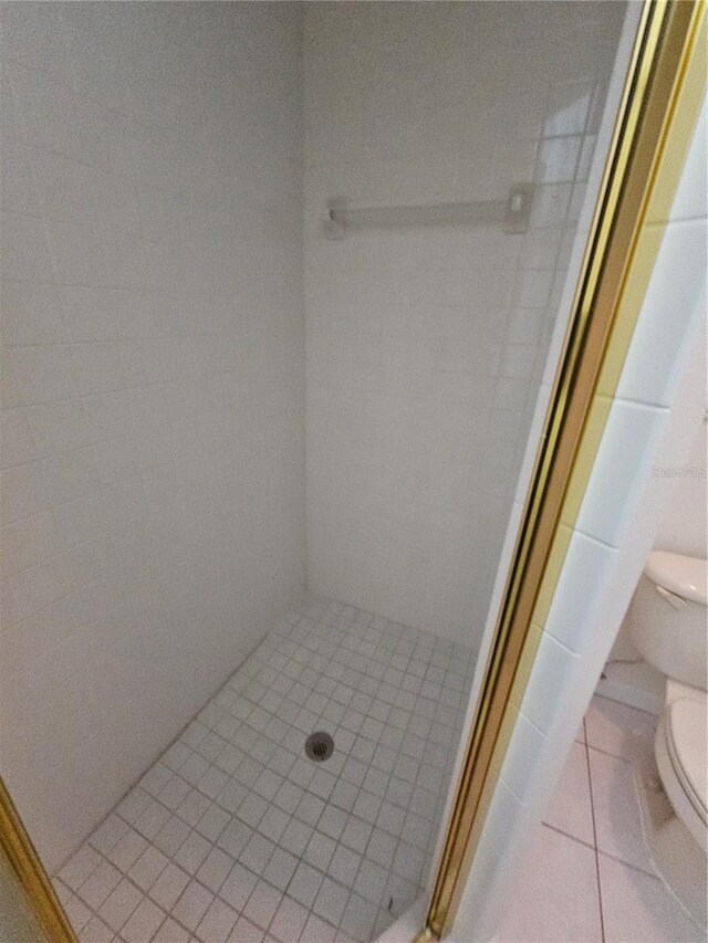 bathroom featuring toilet, a tile shower, and tile patterned flooring