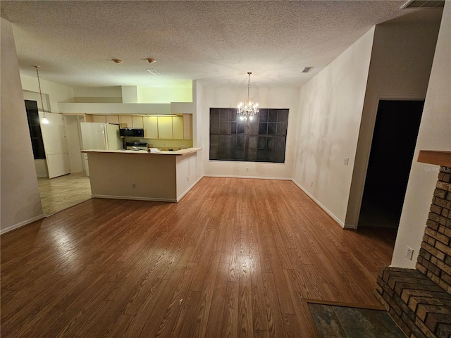 kitchen with white fridge, hardwood / wood-style floors, an inviting chandelier, and kitchen peninsula