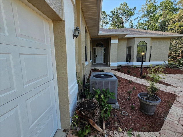 property entrance featuring roof with shingles, central AC unit, and stucco siding