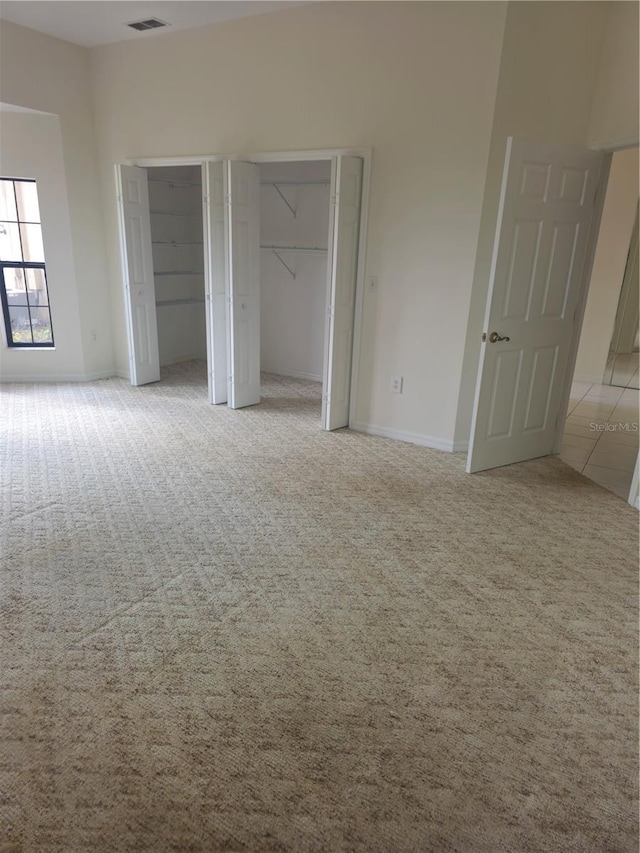 unfurnished bedroom with light carpet, visible vents, baseboards, and two closets