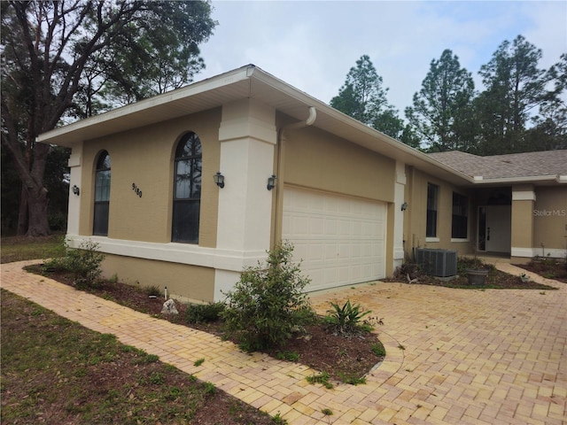 view of side of home with a garage, decorative driveway, central AC, and stucco siding