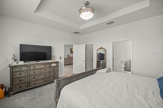 carpeted bedroom with a tray ceiling, connected bathroom, and a chandelier